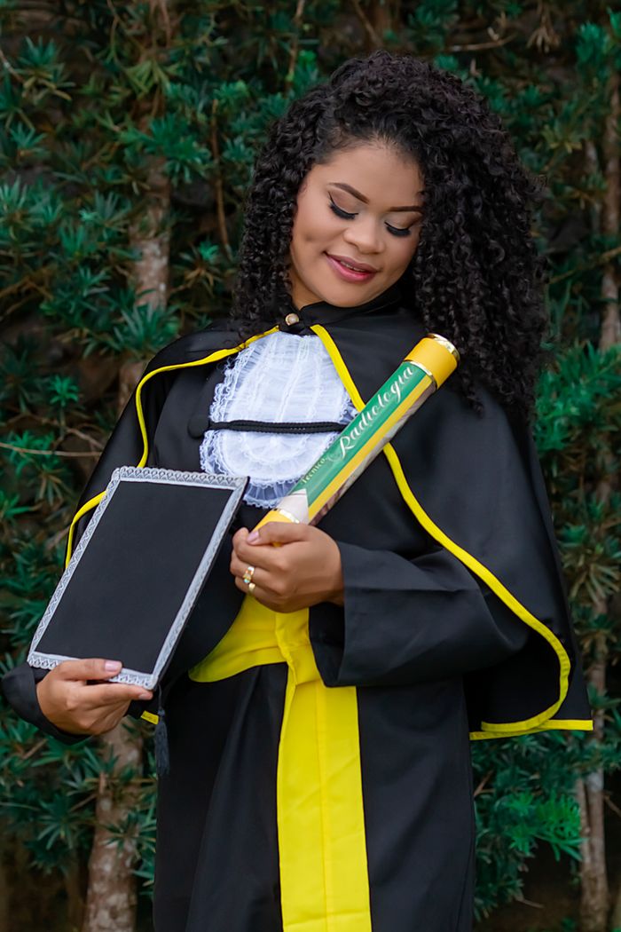 A woman in a graduation gown celebrating her achievement proudly outdoors.