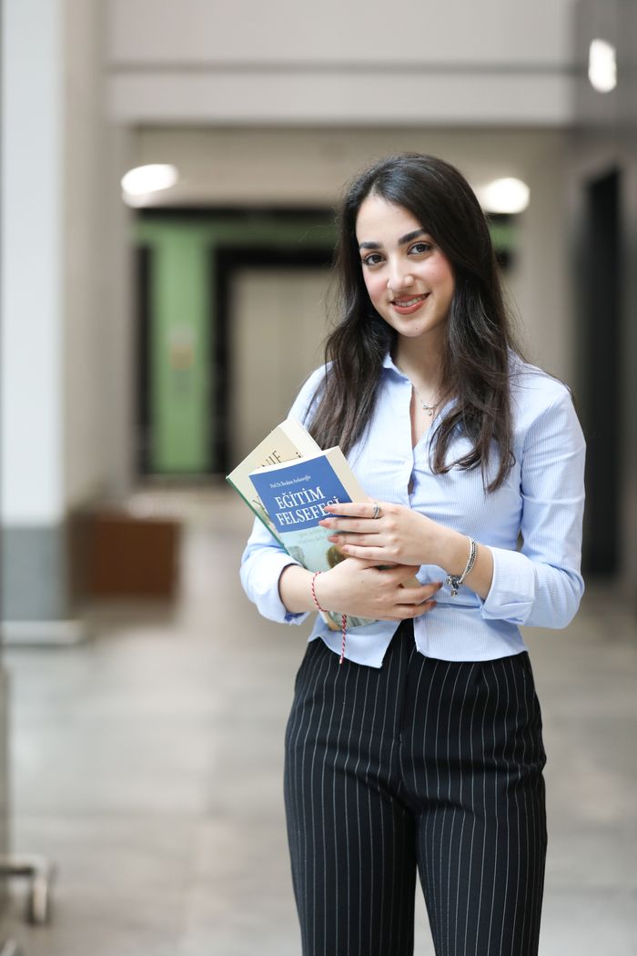 Young woman standing in a modern office corridor holding books, exuding confidence and professionalism.