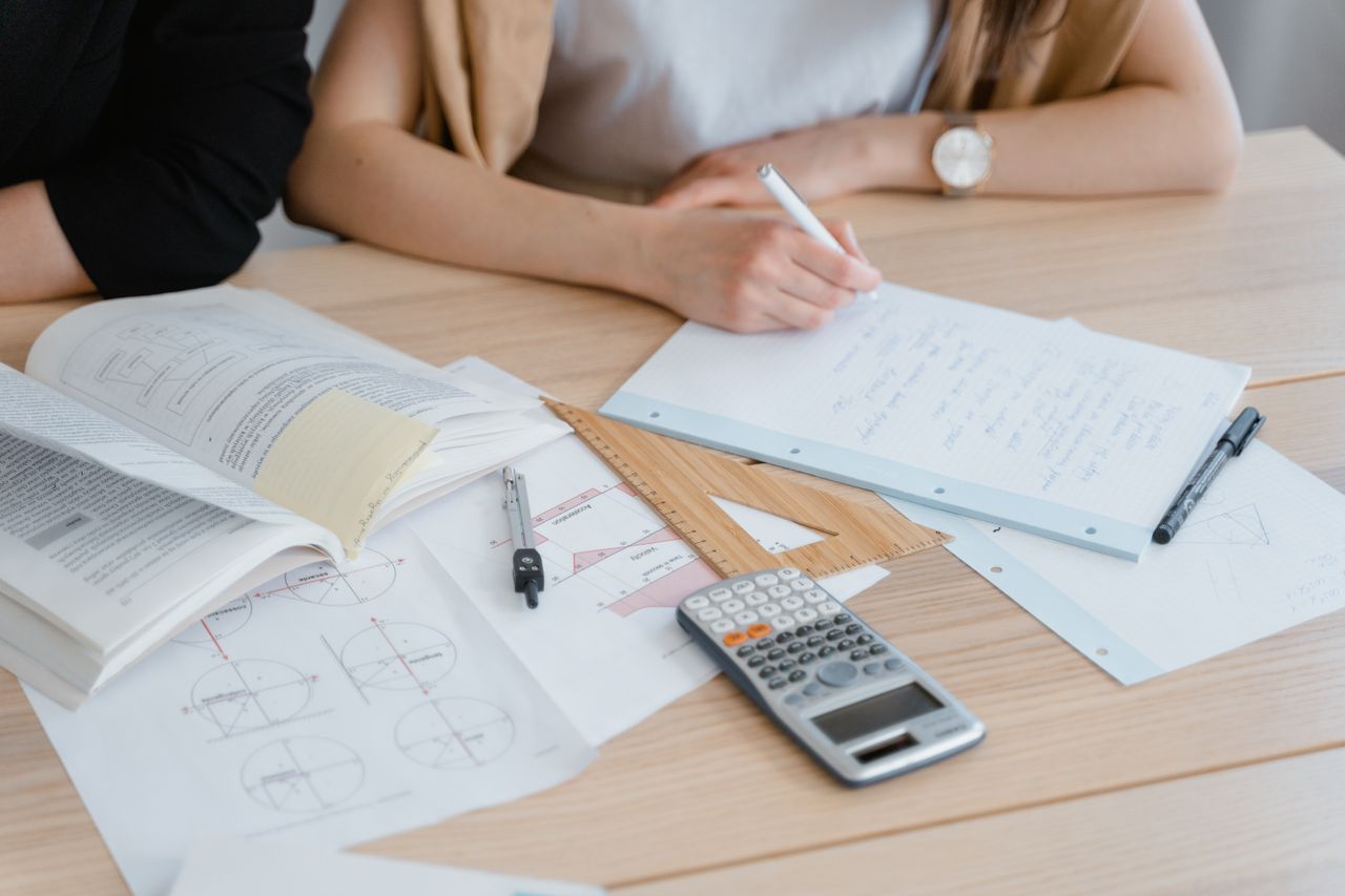 Person writing notes with books and calculator, ideal for study and education themes.
